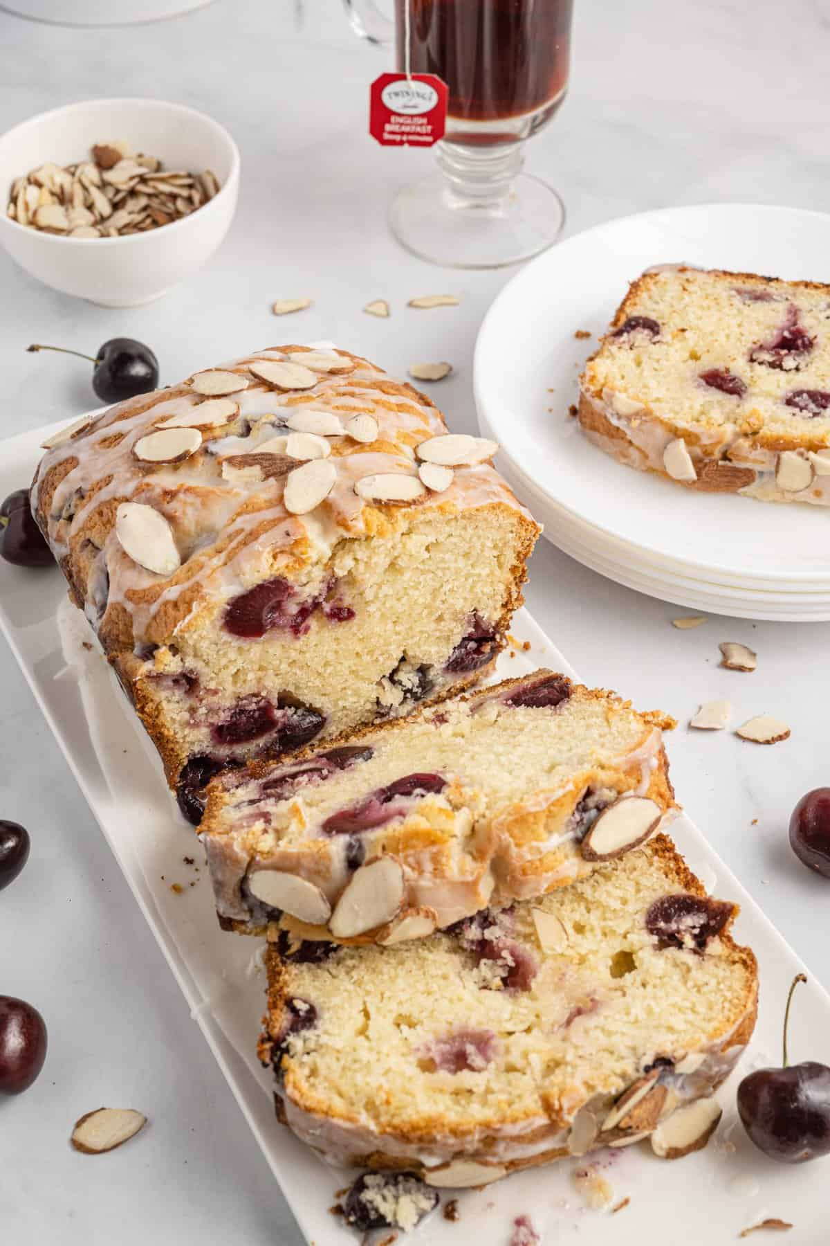 Partially sliced cherry bread on white plate with cherries scattered around.