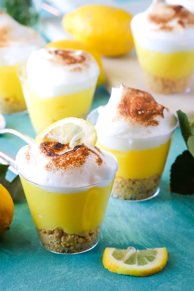 Lemon pudding cups scattered around with lemon slices and whole lemons. 