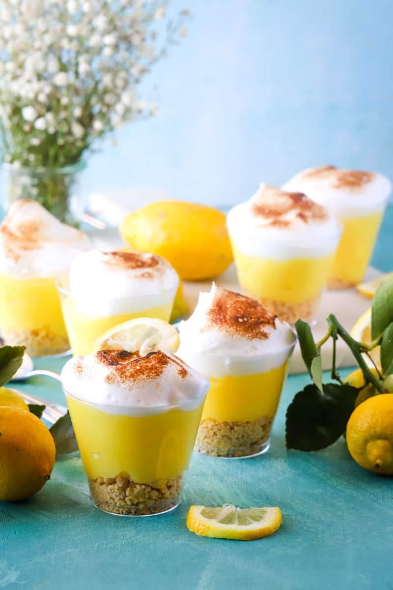 Scattered pudding cups on blue background with fresh lemons and flowers.