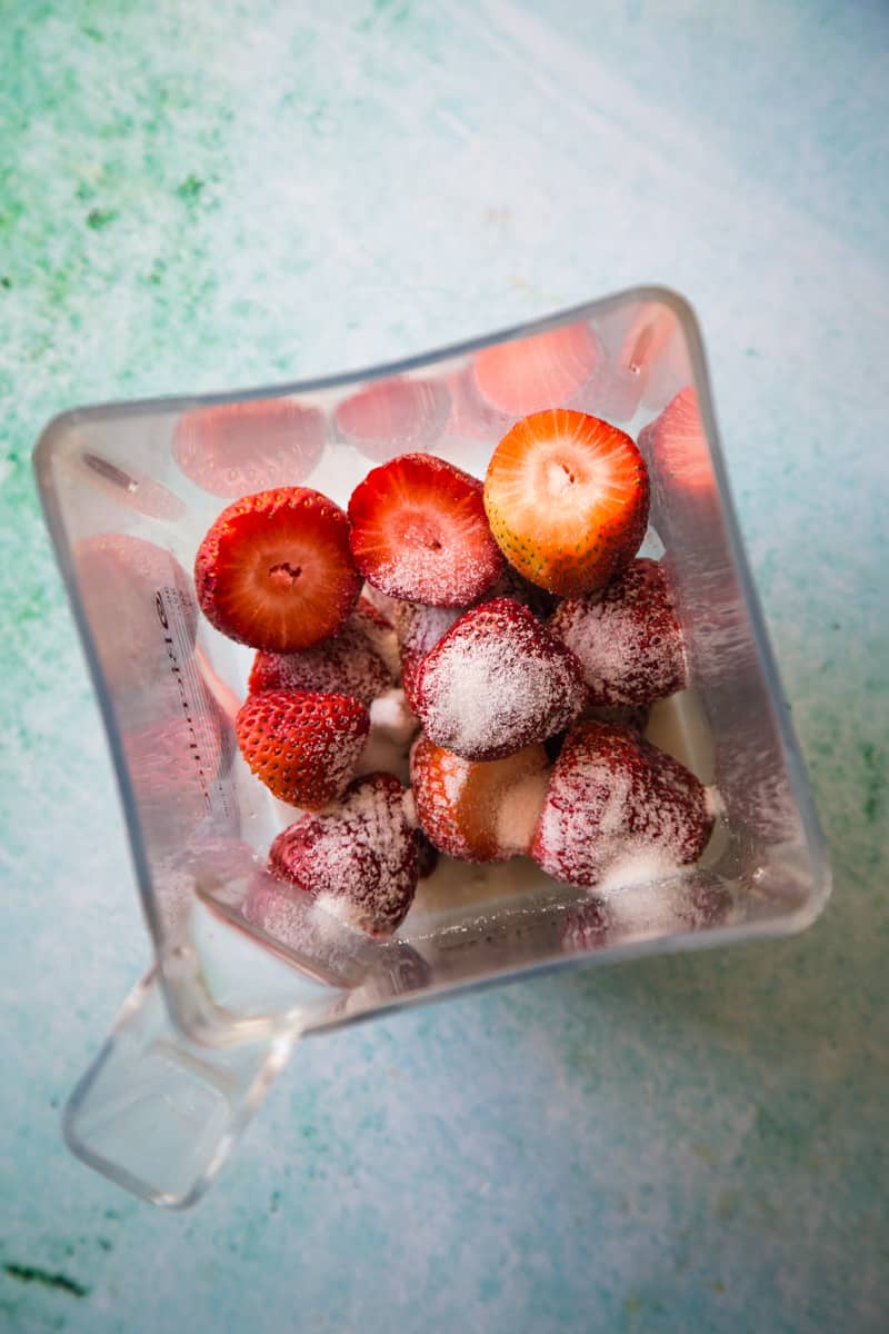 Adding strawberries and sugar to the blender to puree.