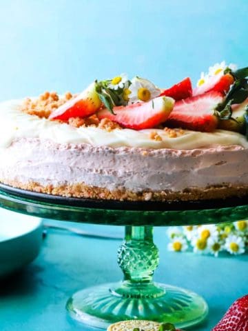 Strawberry shortcake cheesecake recipe on green cake plate garnished with strawberries.