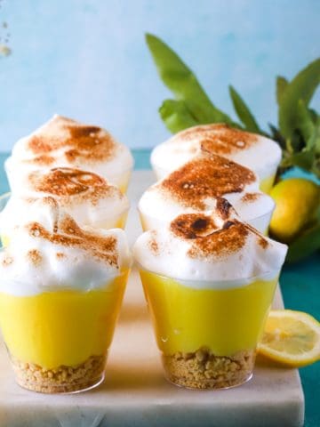 Lemon meringue pudding cups on white marble and teal background.