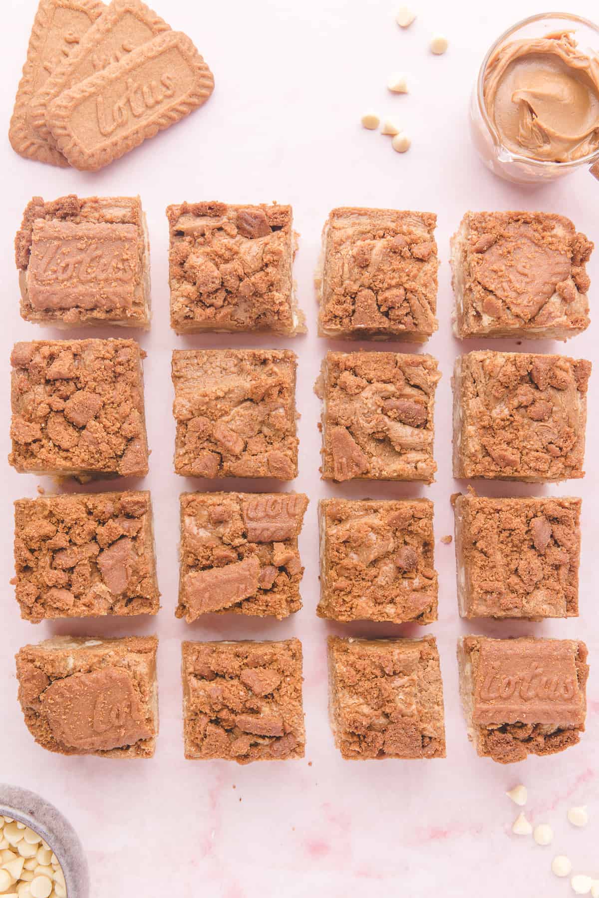 Cookie butter bars cut into 16 squares on pink background. 