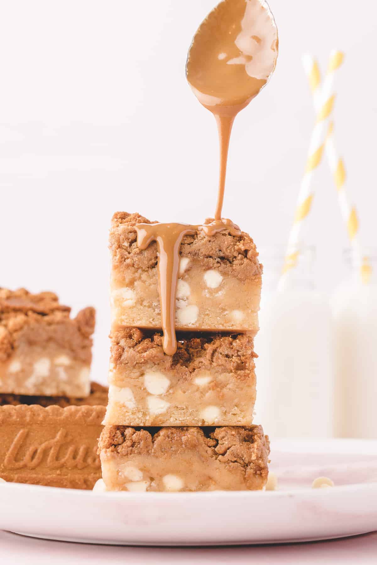 Hand pouring a spoon of biscoff spread over 3 stacked bars. 