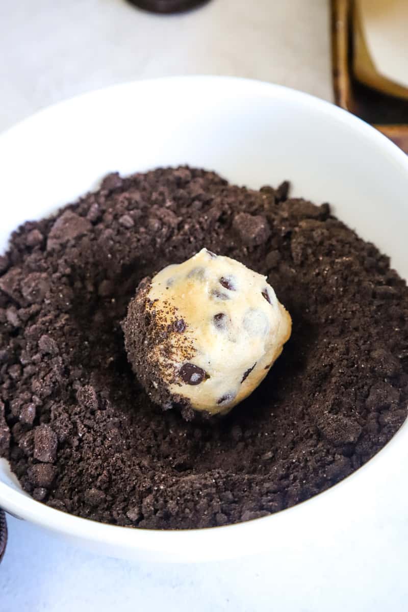 Placing the cookie dough ball in a bowl of crushed Oreos.