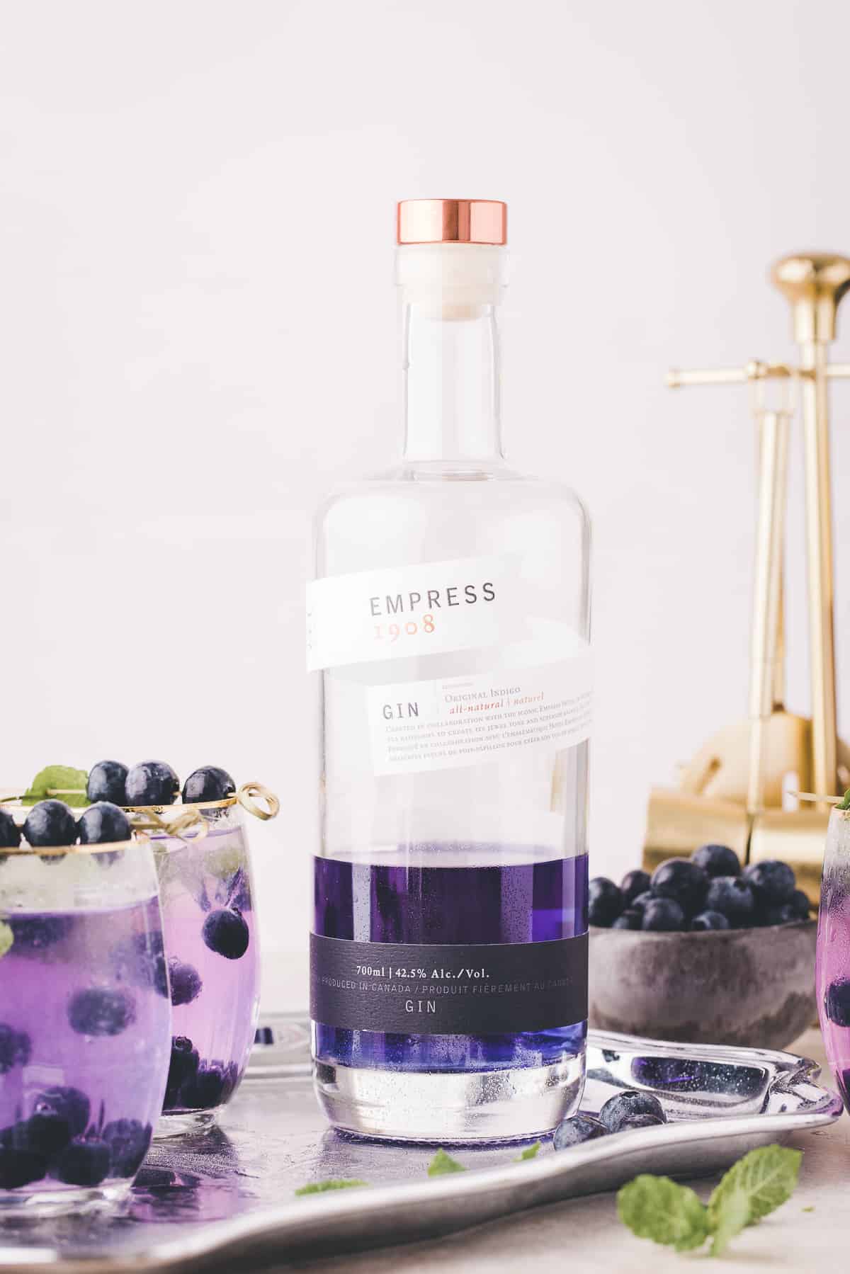 Bottle of purple empress gin with cocktails next to it.