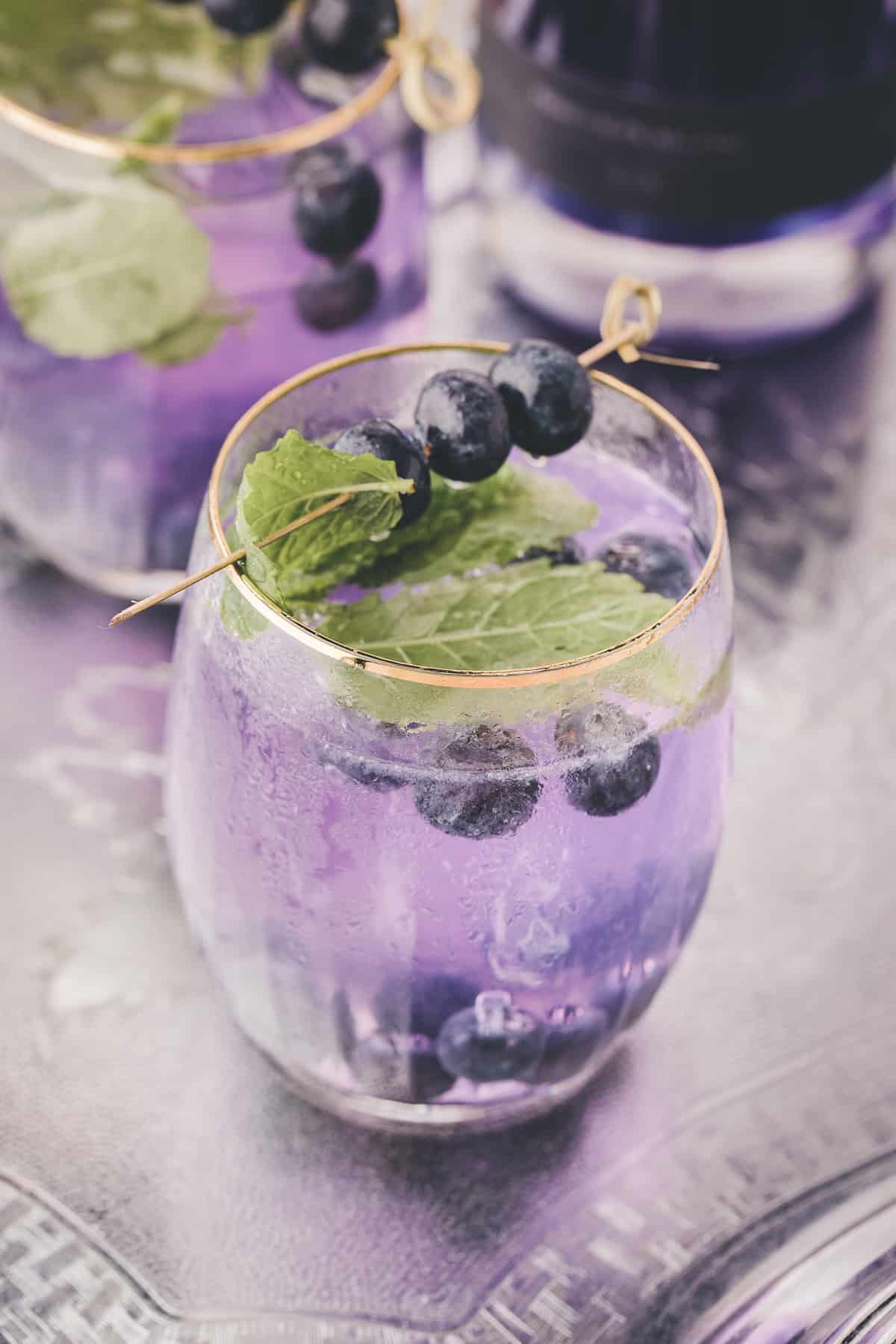 two mint and blueberry cocktails on metal serving dish.