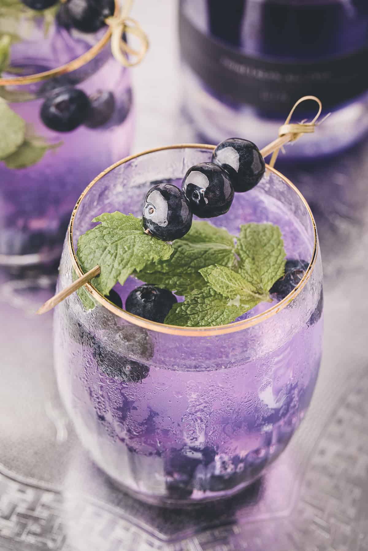close up shot of the purple cocktail with blueberry and mint skewers.