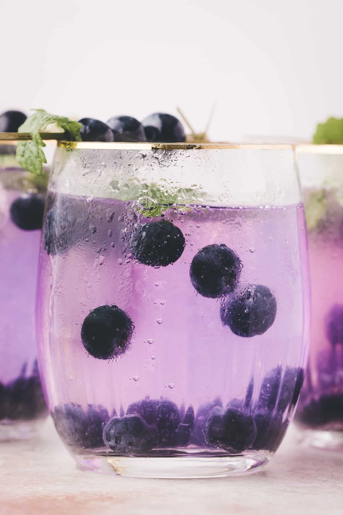 unclose photo of the purple cocktail with blueberries floating in the drink.
