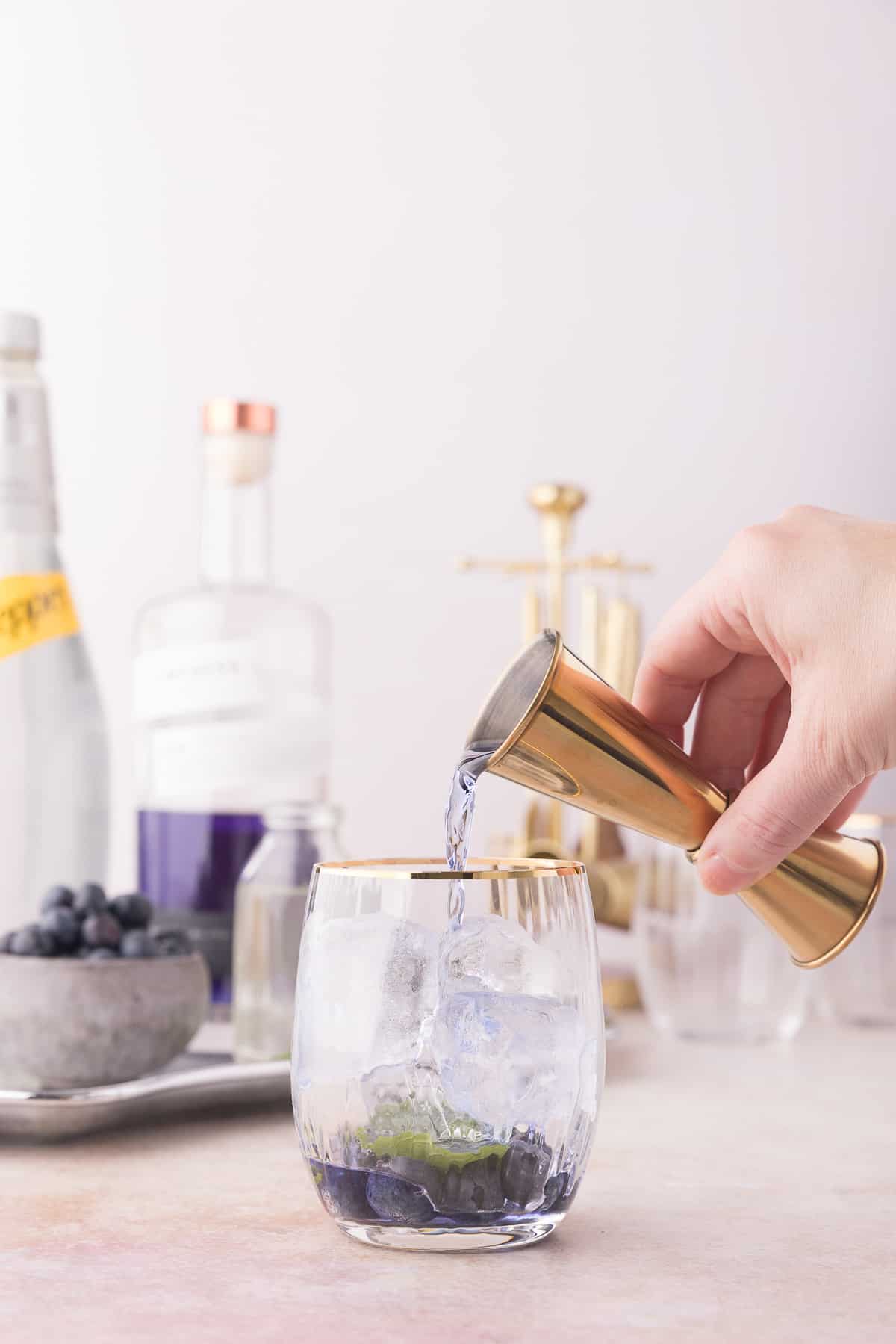 Hand pouring the blue hued empress gin into the cocktail glass.