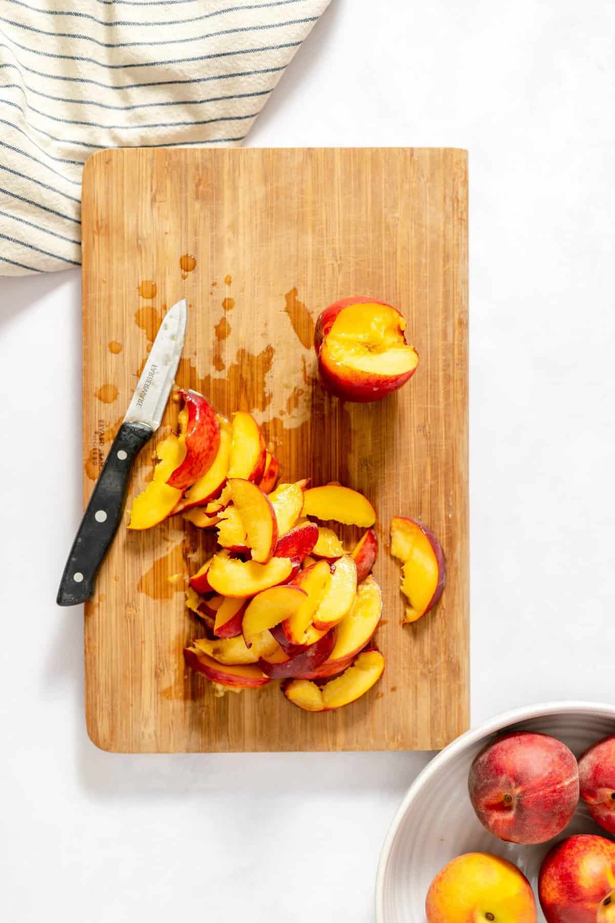 wooden cutting board with knife and sliced peaches.