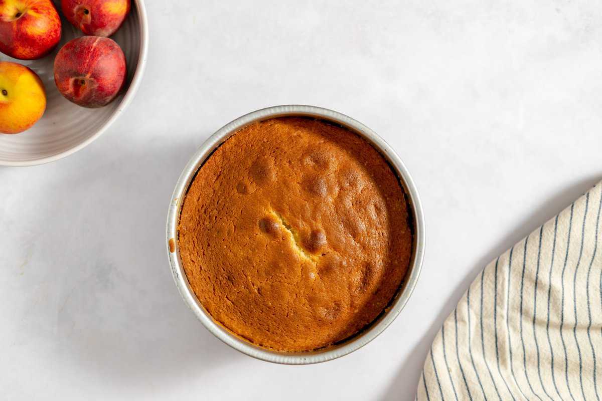 baked cake in cake pan on white background and fresh peaches in bowl.