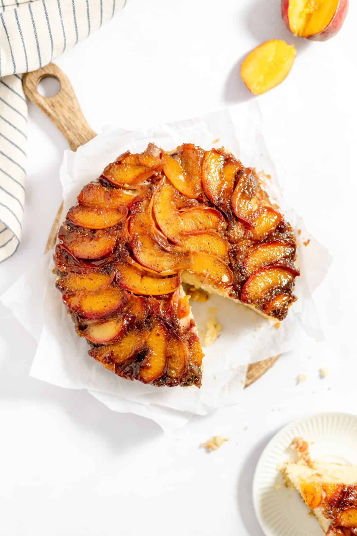 whole peach upside down cake on wooden cutting board with slice removed.
