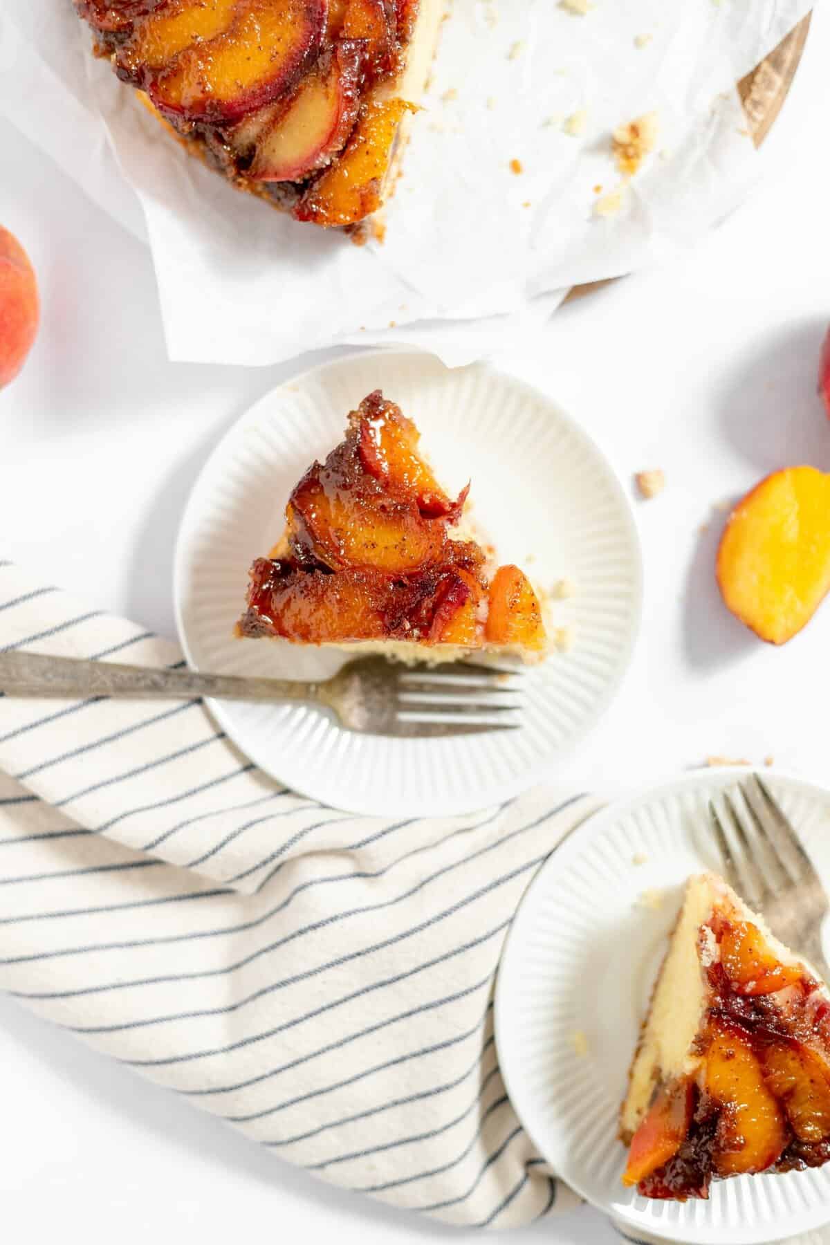 two slices of peach upside down cake on white plates with forks.
