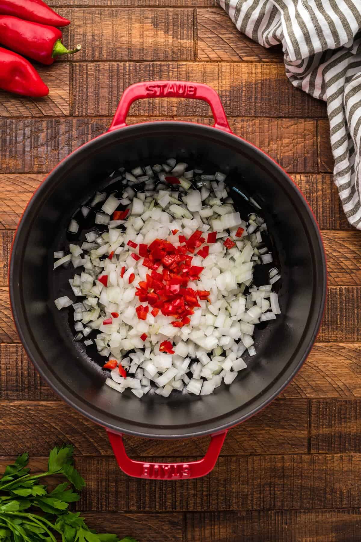 red pot with onions and chopped chili peppers on wood background.
