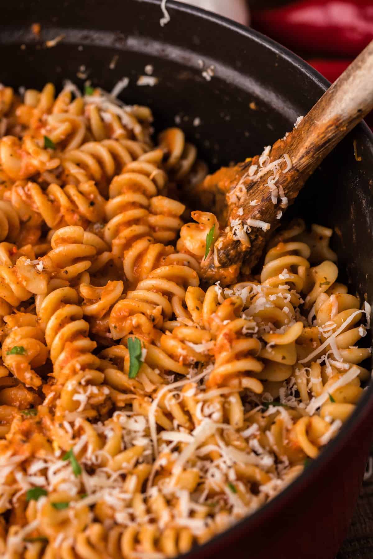 Side shot of the pot of spicy fusilli pasta with wooden spoon.