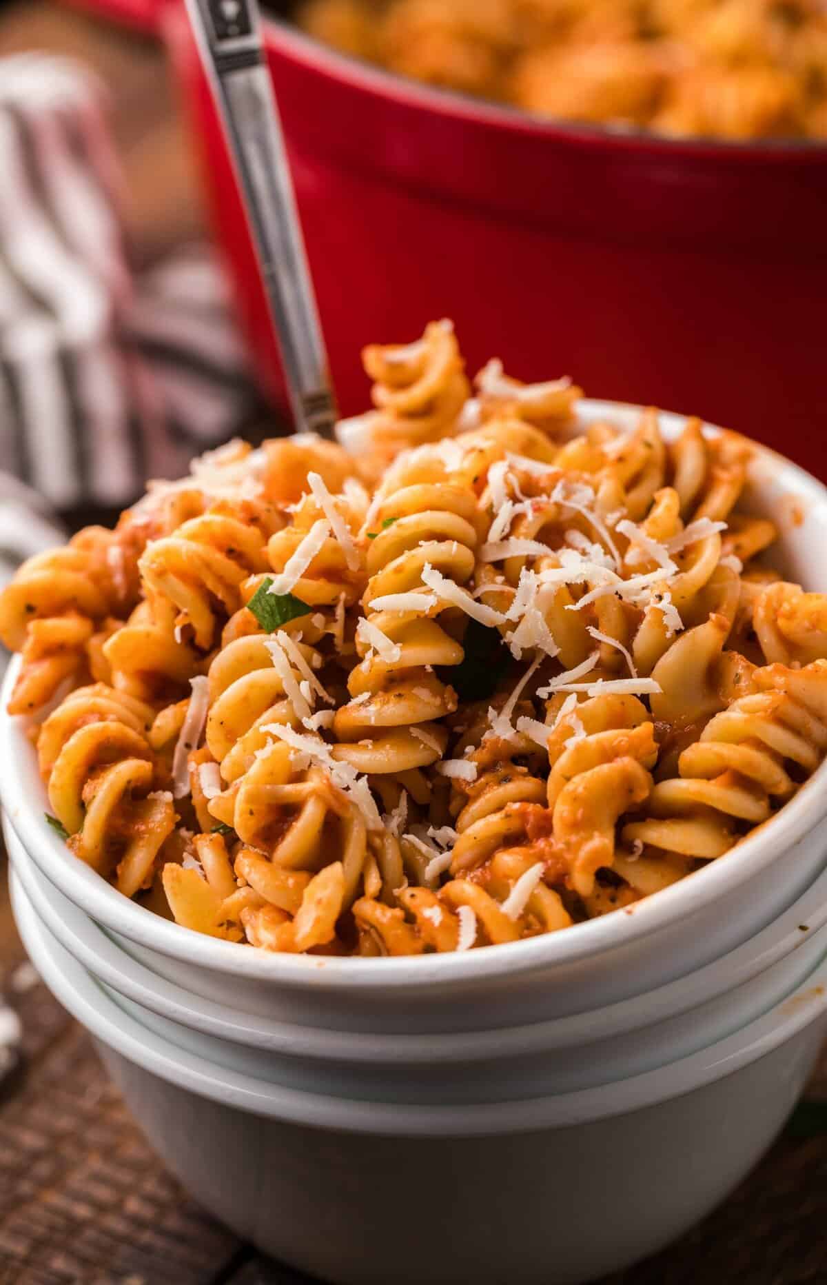 Spicy fusilli pasta with grated parmesan cheese in a white bowl.