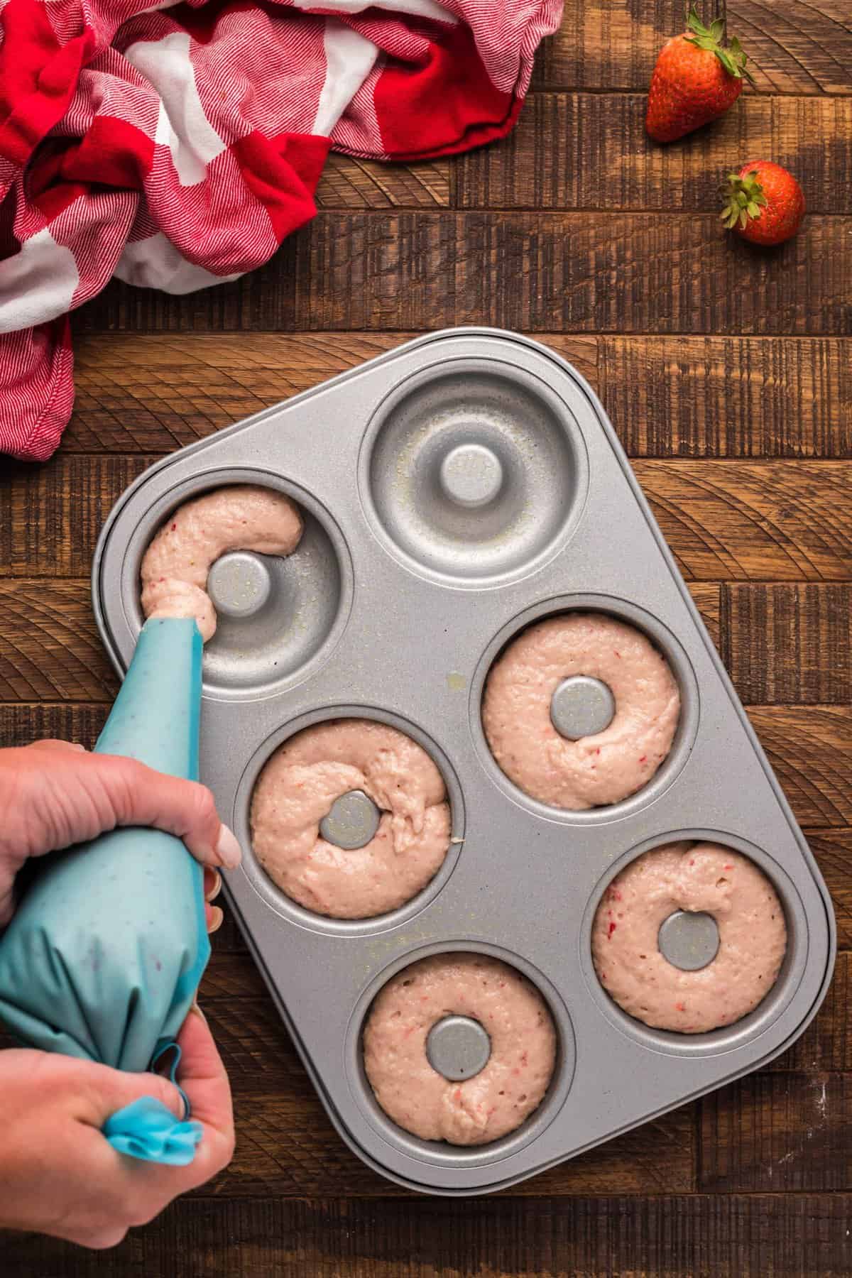 Hand piping the donut batter into the donut pans.