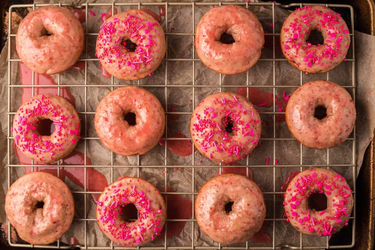 Horizontal shot of strawberry donuts with pink sprinkles on wire rack.