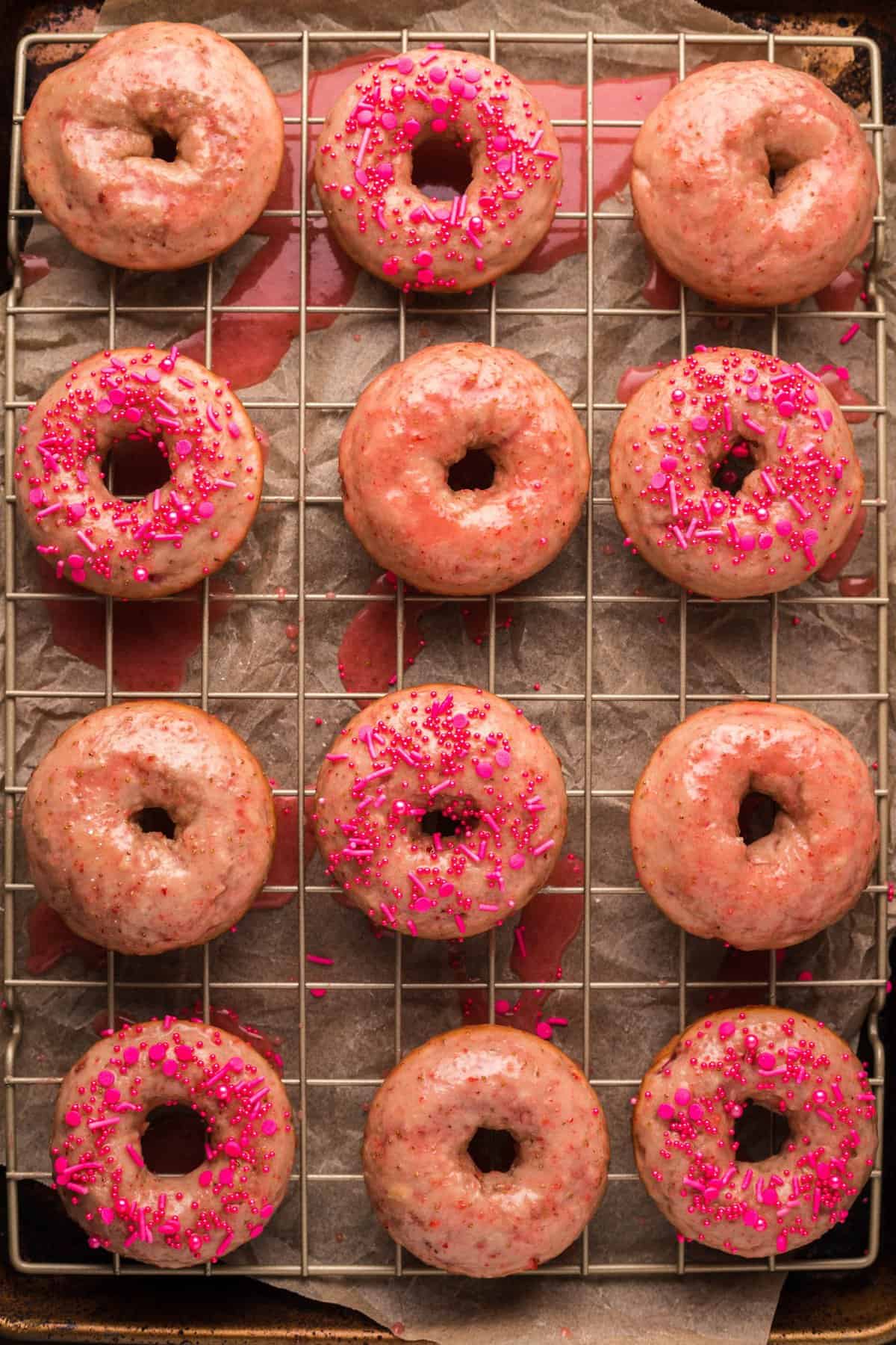 Vertical overhead shot of donuts with pink sprinkles on wire cooling rack.