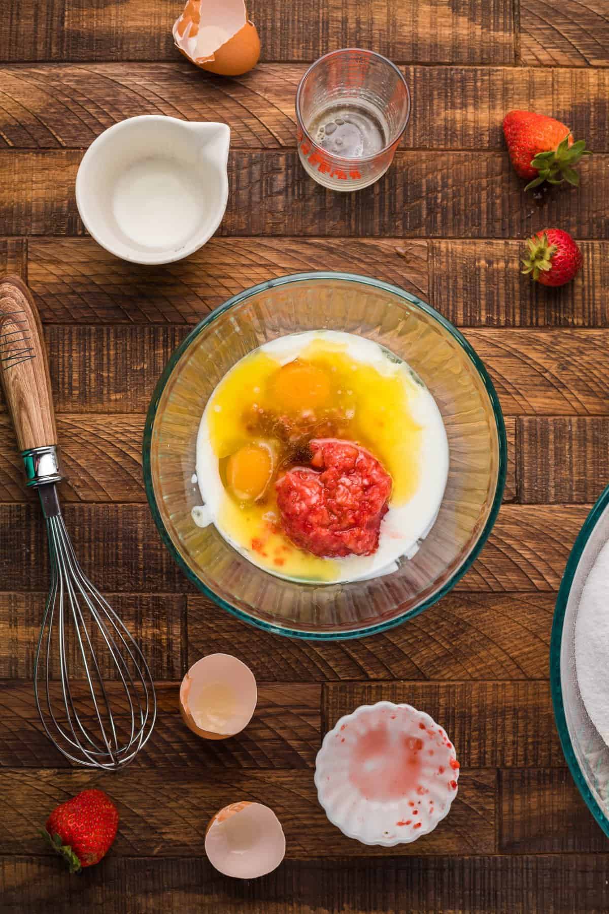 Eggs, sugar, and strawberry puree in a large glass bowl with whisk.