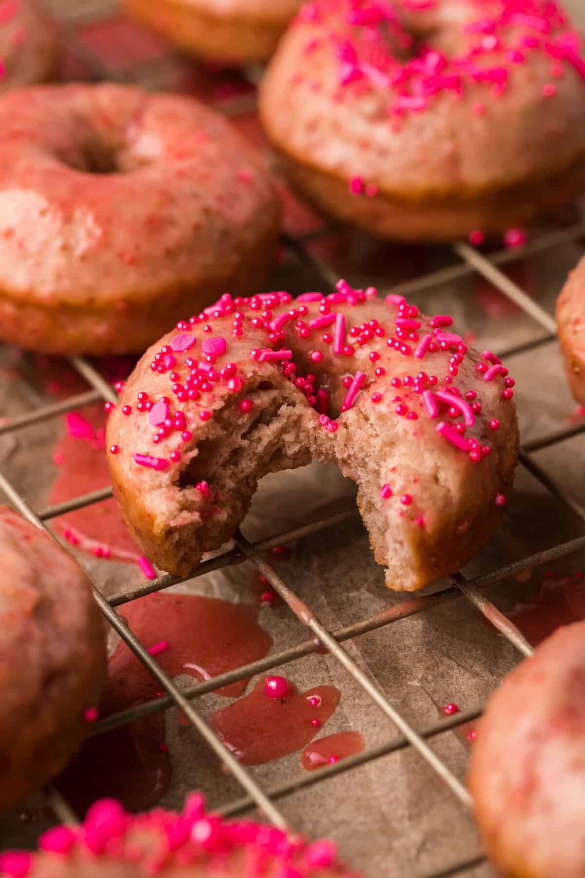 Glazed strawberry donut with sprinkles and bite taken out of donut.
