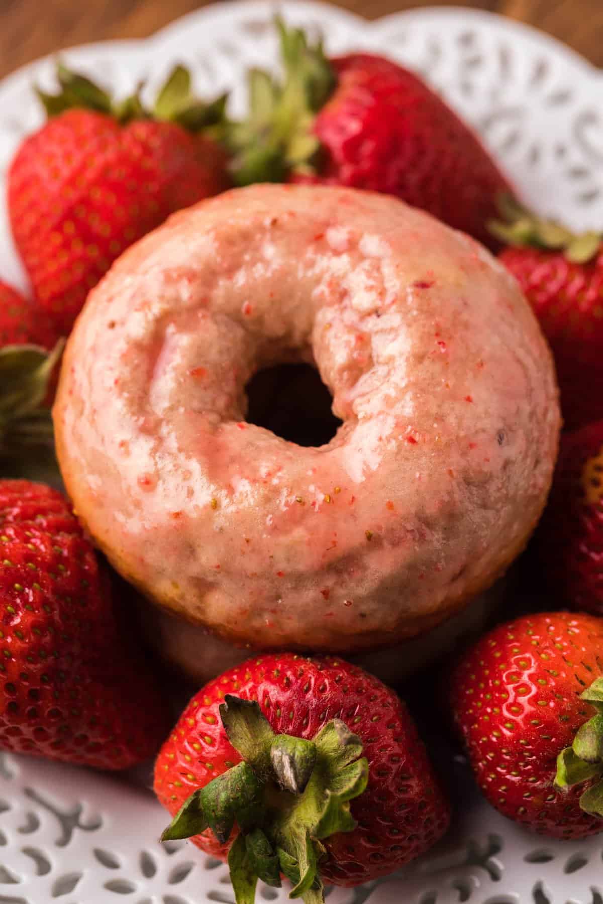 Pink donut surrounded by fresh strawberries on white plate.