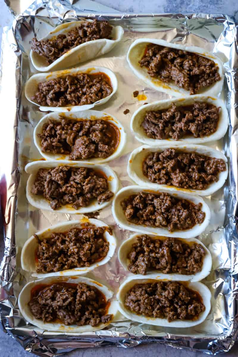 Filling the unbaked taco boats with hamburger meat with enchilada sauce. 