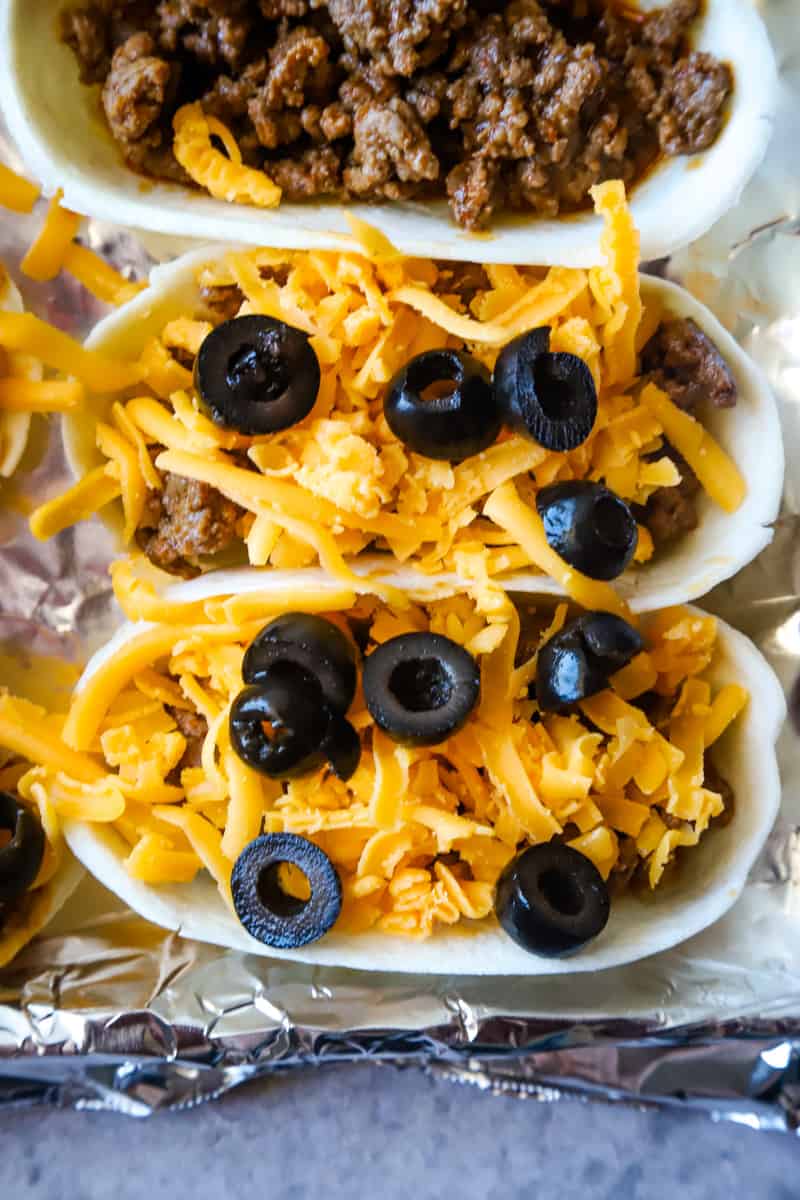 Topping the meat in the taco boats with shredded cheese and sliced olives. 