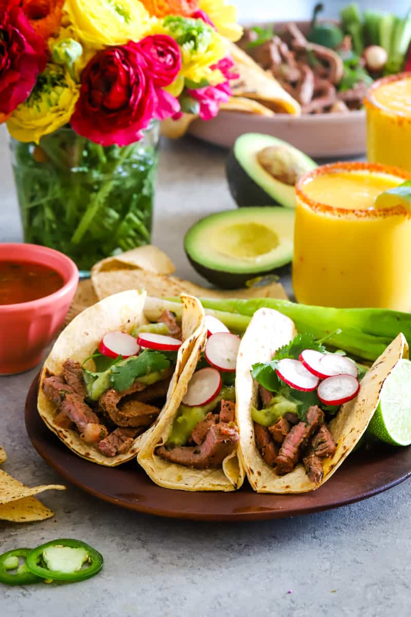 Carne asada tacos on plate with mango margaritas in the background. 