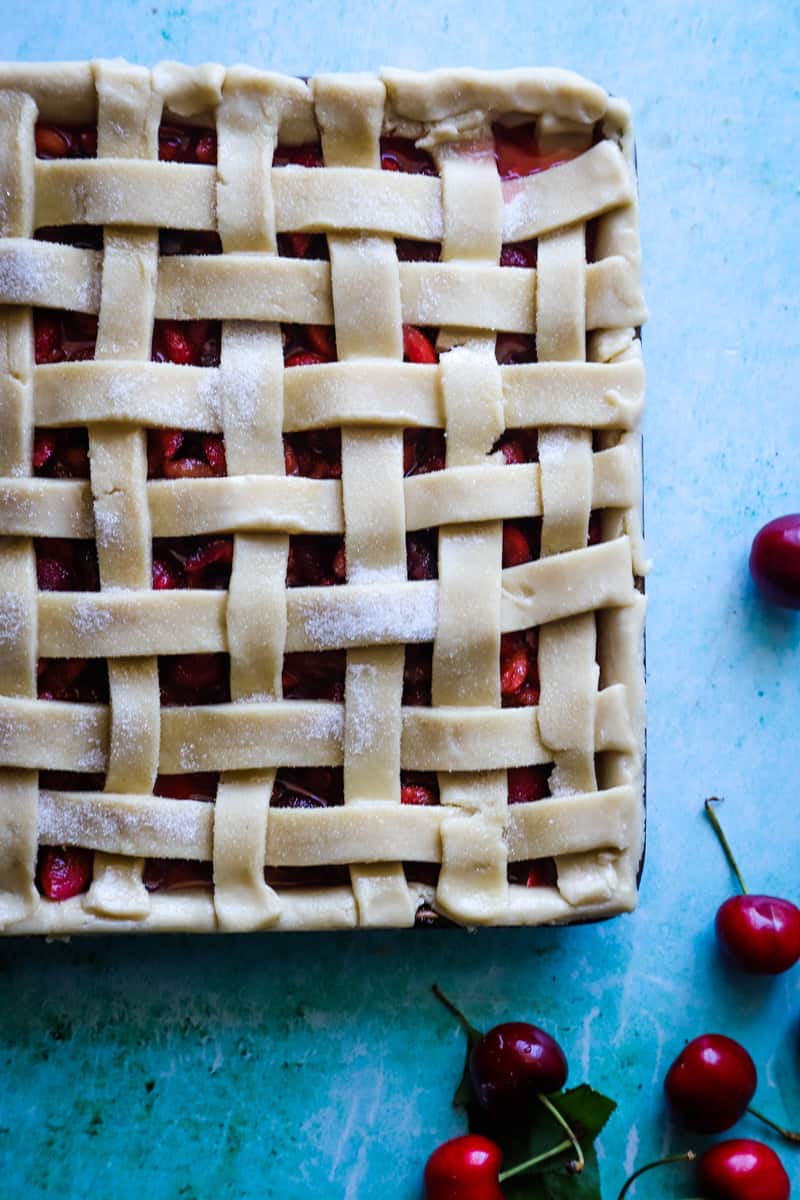 The unbaked cherry slab pie with lattice crust with edges trimmed and fresh cherries on the side. 