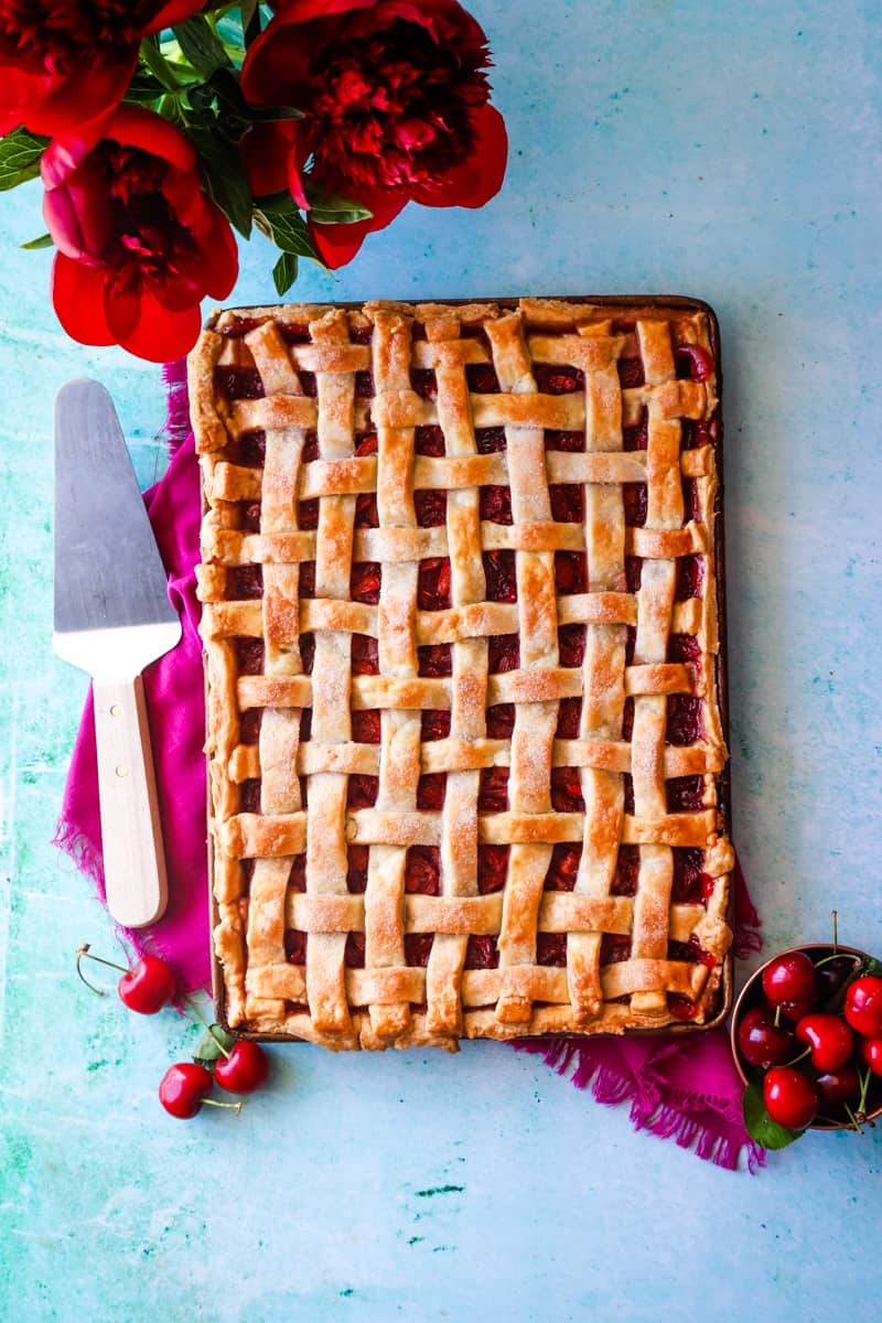 Overhead shot of the cherry slab pie with lattice crust on a blue background with red flowers. 