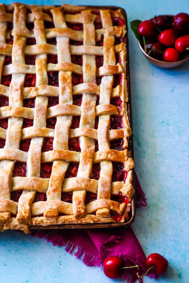 Half of the baked cherry pie with golden lattice crust on blue background with pink dishtowel underneath. 