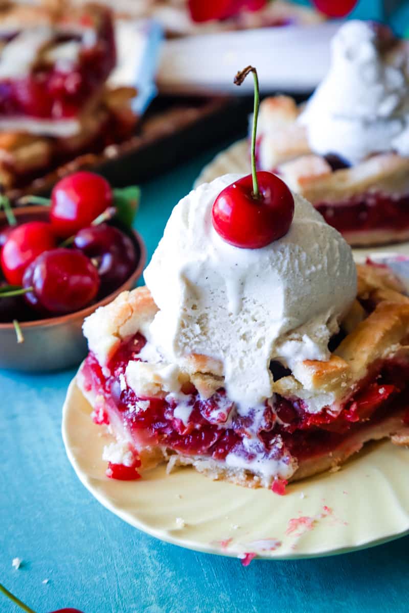 Cherry pie square with ice cream scooped on top with piece taken out. 