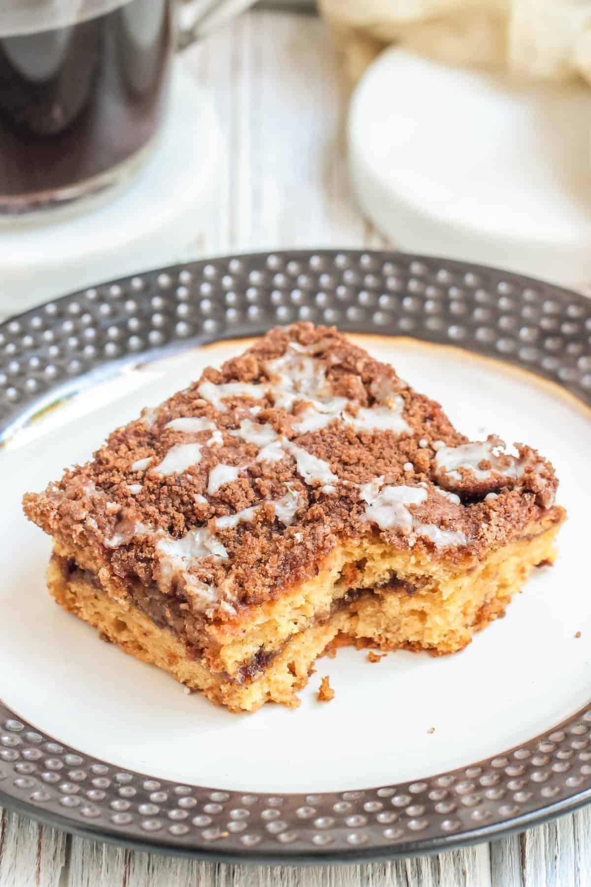 Slice of coffee cake with bite taken out on white plate with silver rim