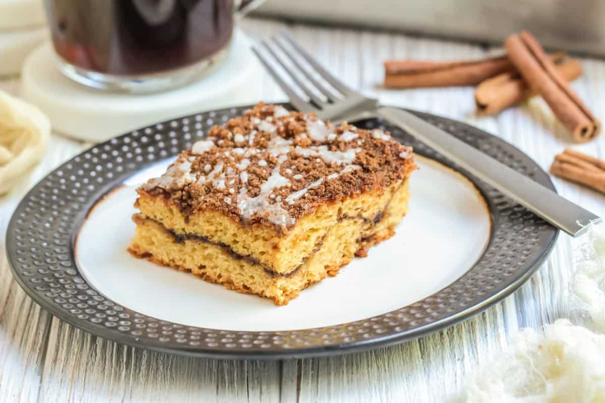 Slice of coffee cake on a white plate with gray rim and a fork on the side. 