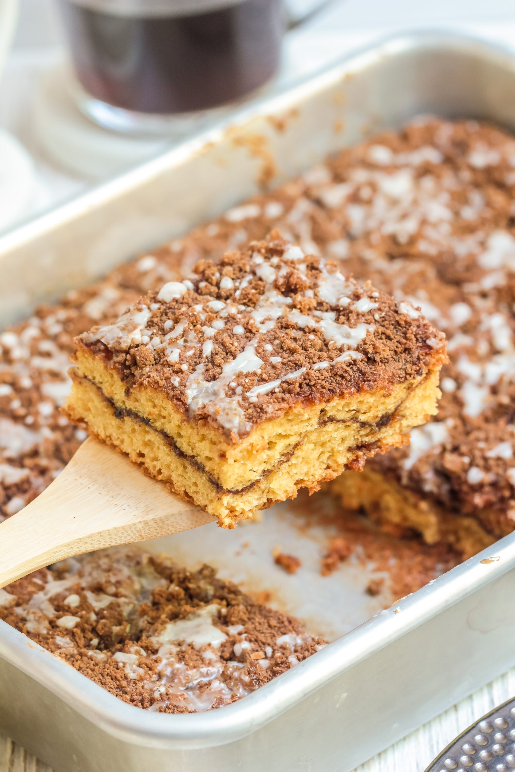 Tray of coffee cake in a white baking dish with a spatula taking a square from it. 