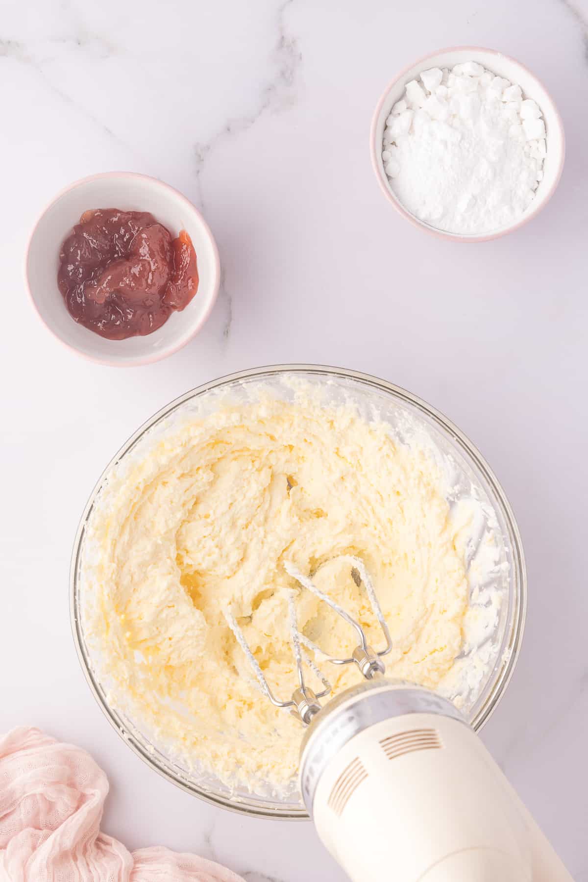 large glass bowl with hand mixer beating butter and cream cheese. 