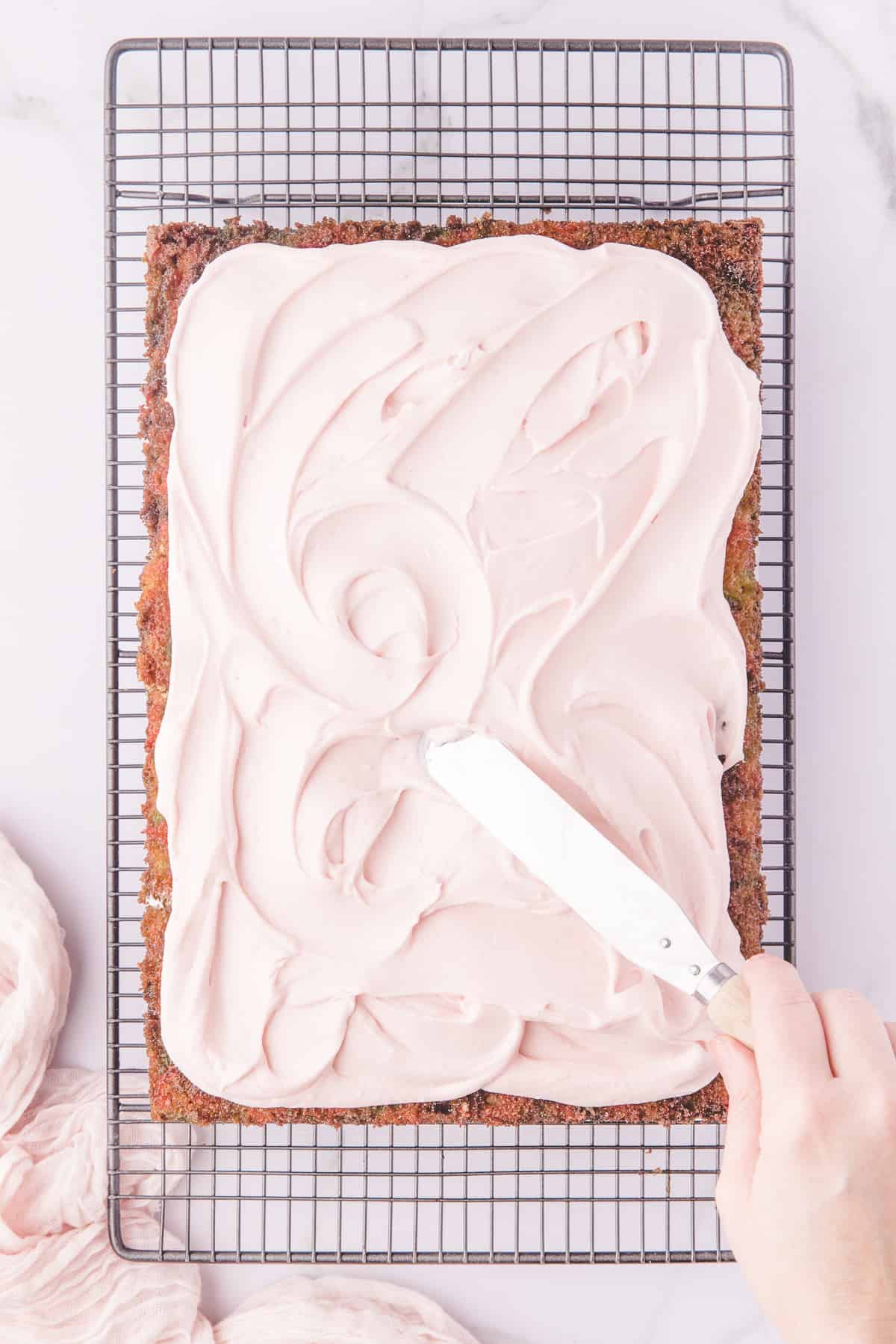 Hand using an offset spatula to swirl frosting over the cake on a wire rack. 