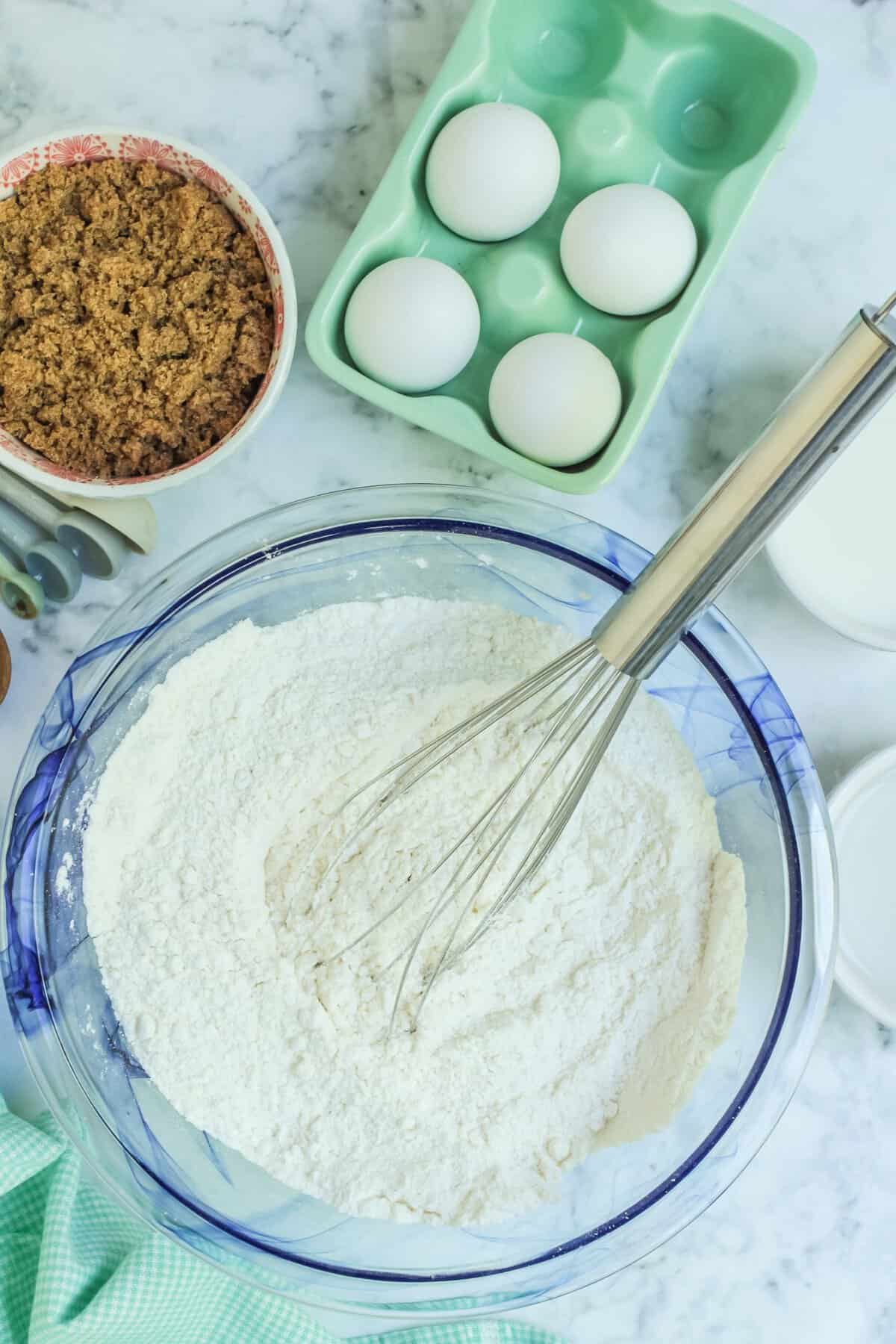 Glass bowl with dry ingredients and a whisk. 