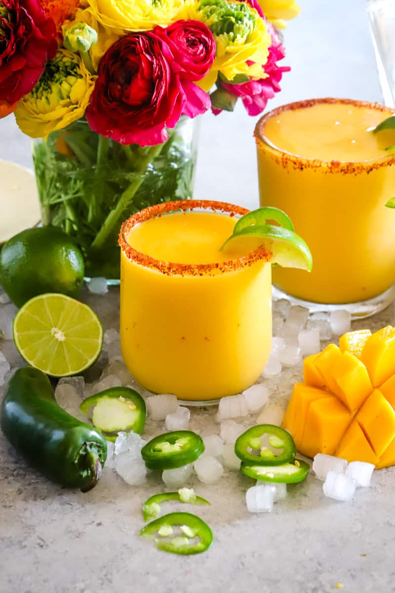 Two glasses filled with mango margaritas and bright flowers in the background. 