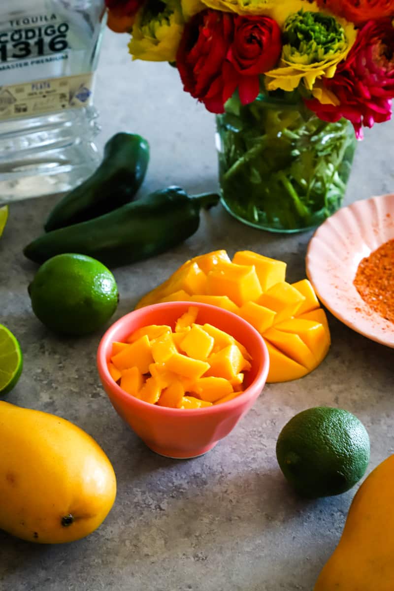 Ingredients to make mango margaritas in small bowls on metal background. 