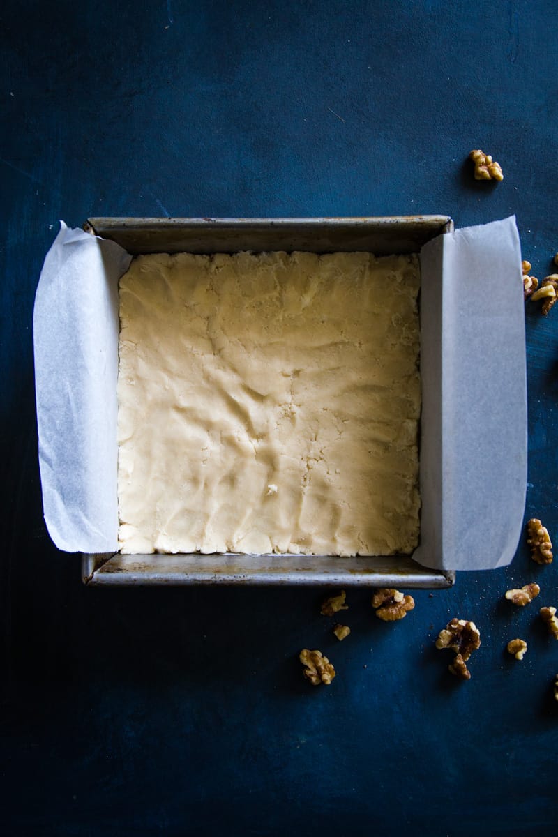Shortbread crust in a parchment lined square pan on blue surface
