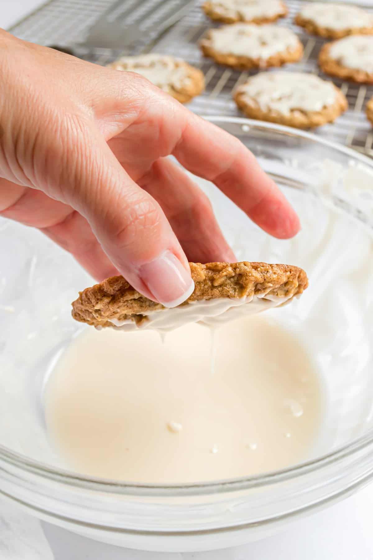 Hand dipping the oatmeal cookie into a bowl with the icing. 