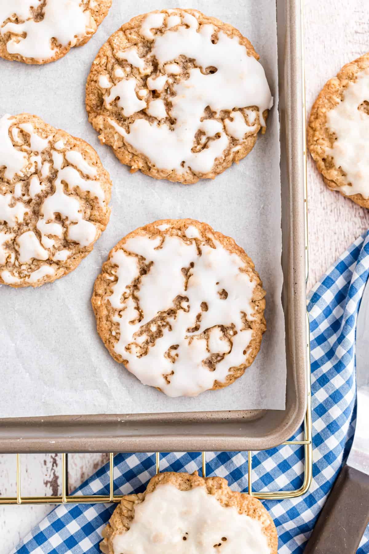 Iced oatmeal cookies on a parchment lined cookie sheet with blue checkered dishtowel underneath. 
