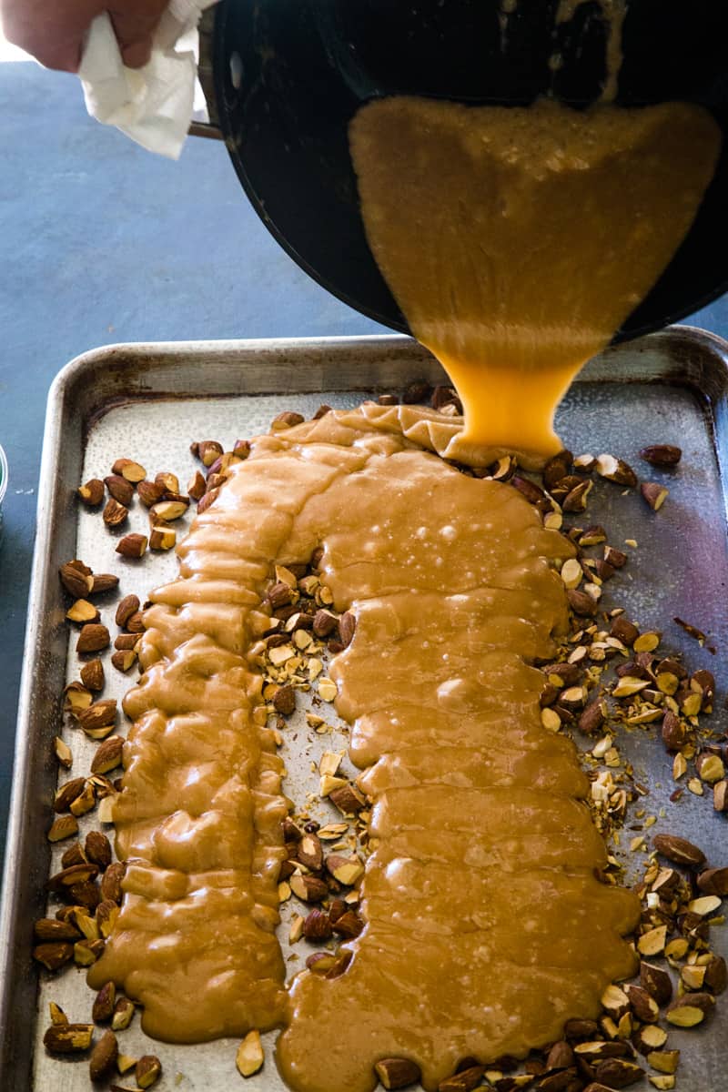 Pouring the hot toffee mixture onto the cookie sheet with almonds. 