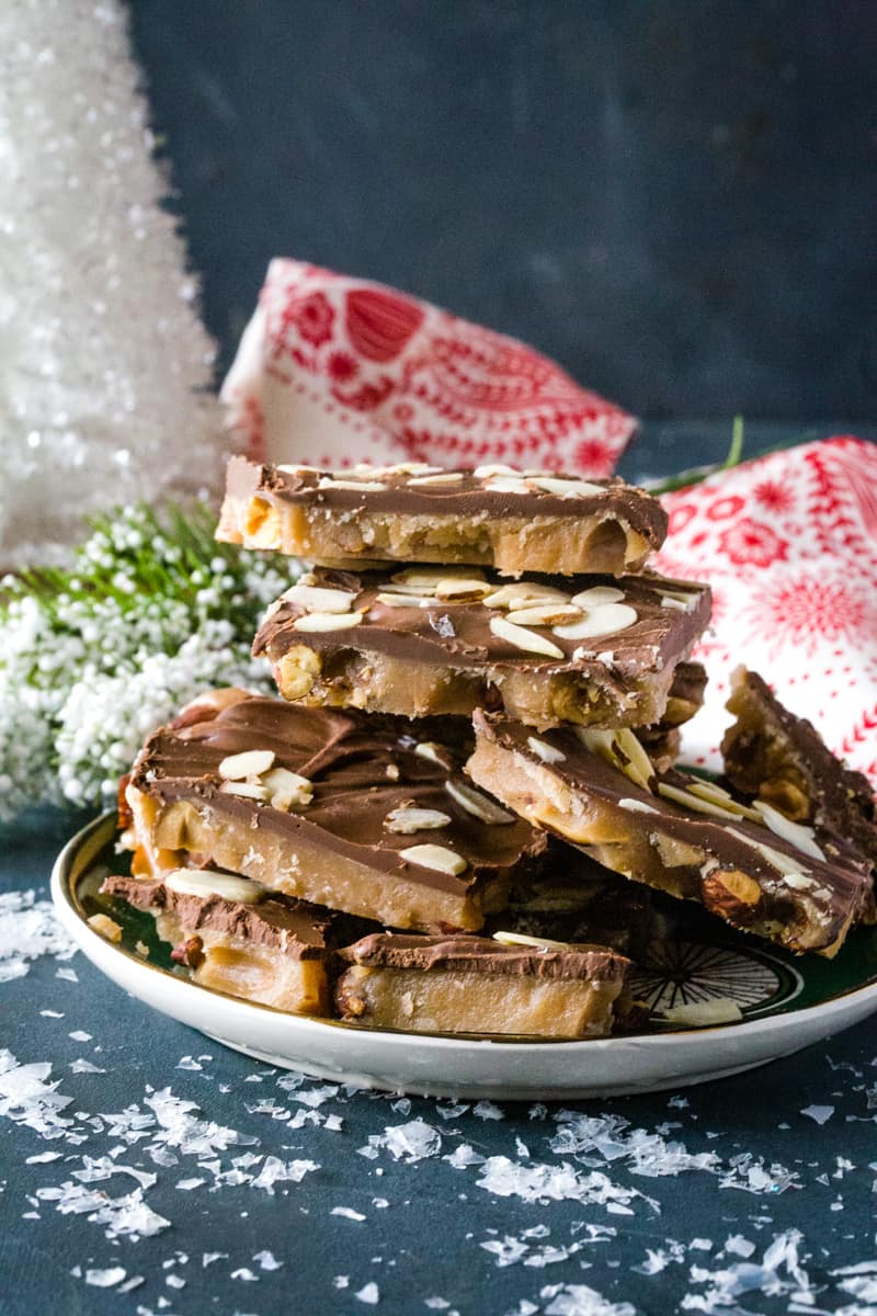 Chunks of English butter toffee layered on a green plate with a white Christmas tree in the background. 