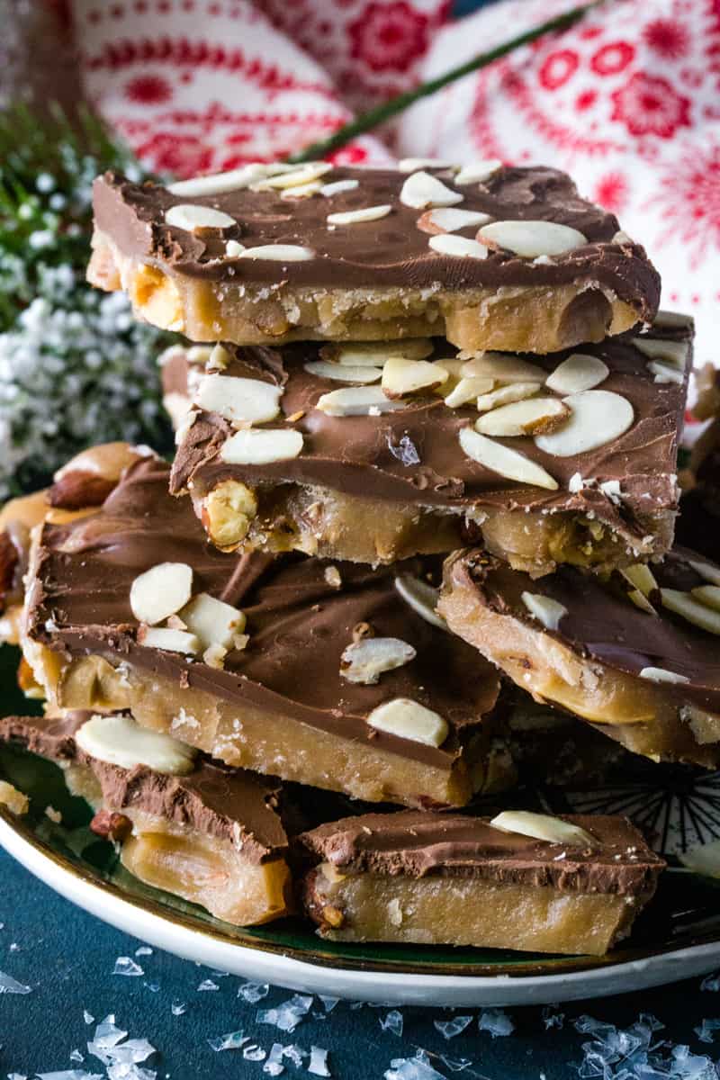 Toffee that is topped with a layer of chocolate and sliced almonds stacked on a green plate. 