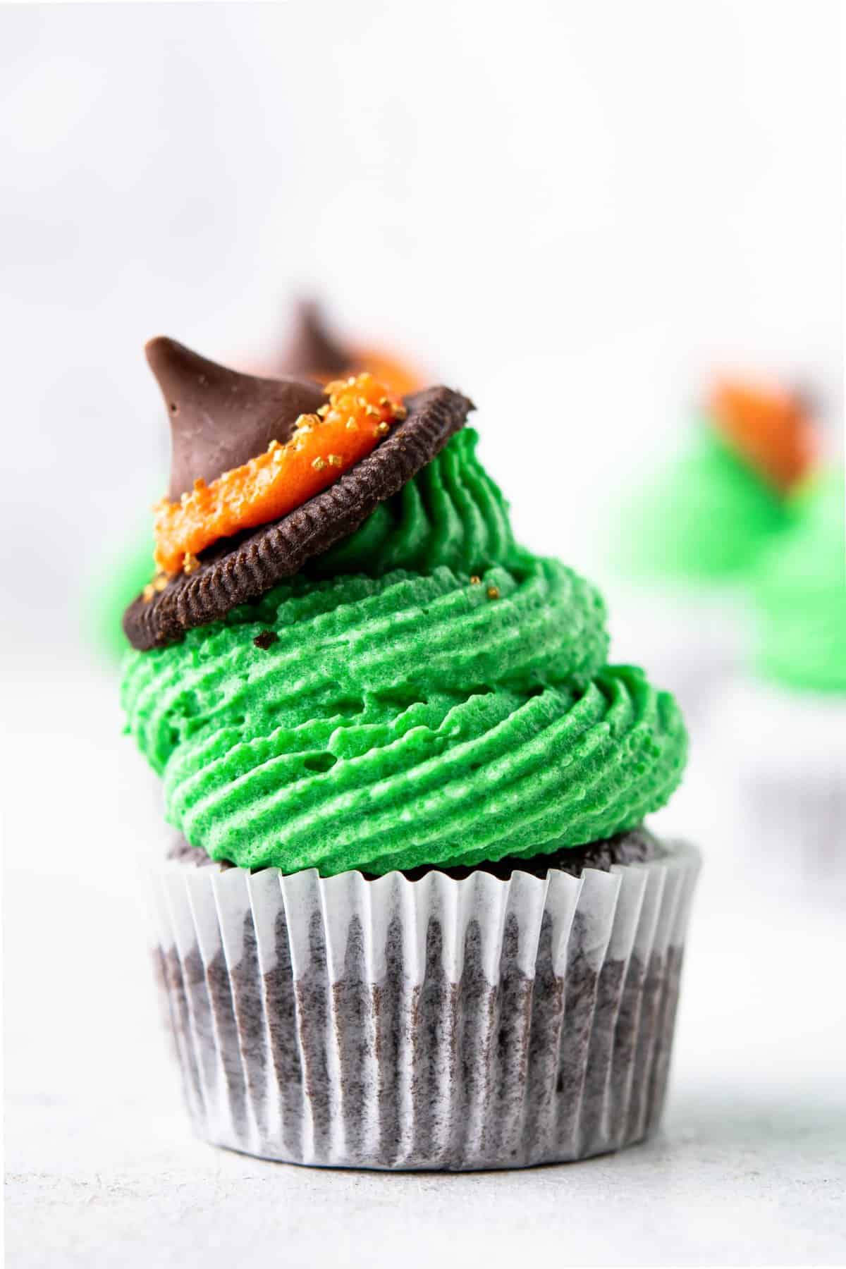 Chocolate cupcake with green frosting and a witch hat topping on white background. 