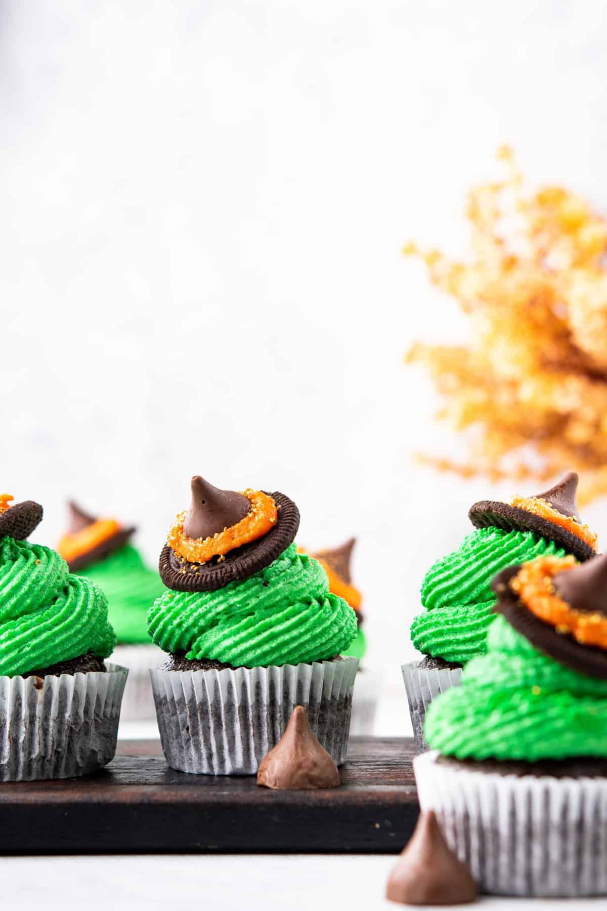 Witch hat cupcakes on black tray with brown foliage in background. 